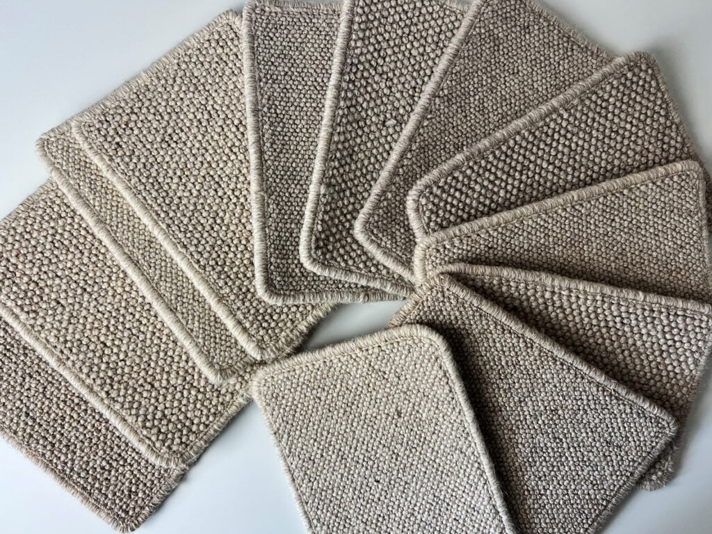 Assorted neutral wool carpet swatches in beige and taupe tones arranged in a fan layout, reflecting neutral home trends.