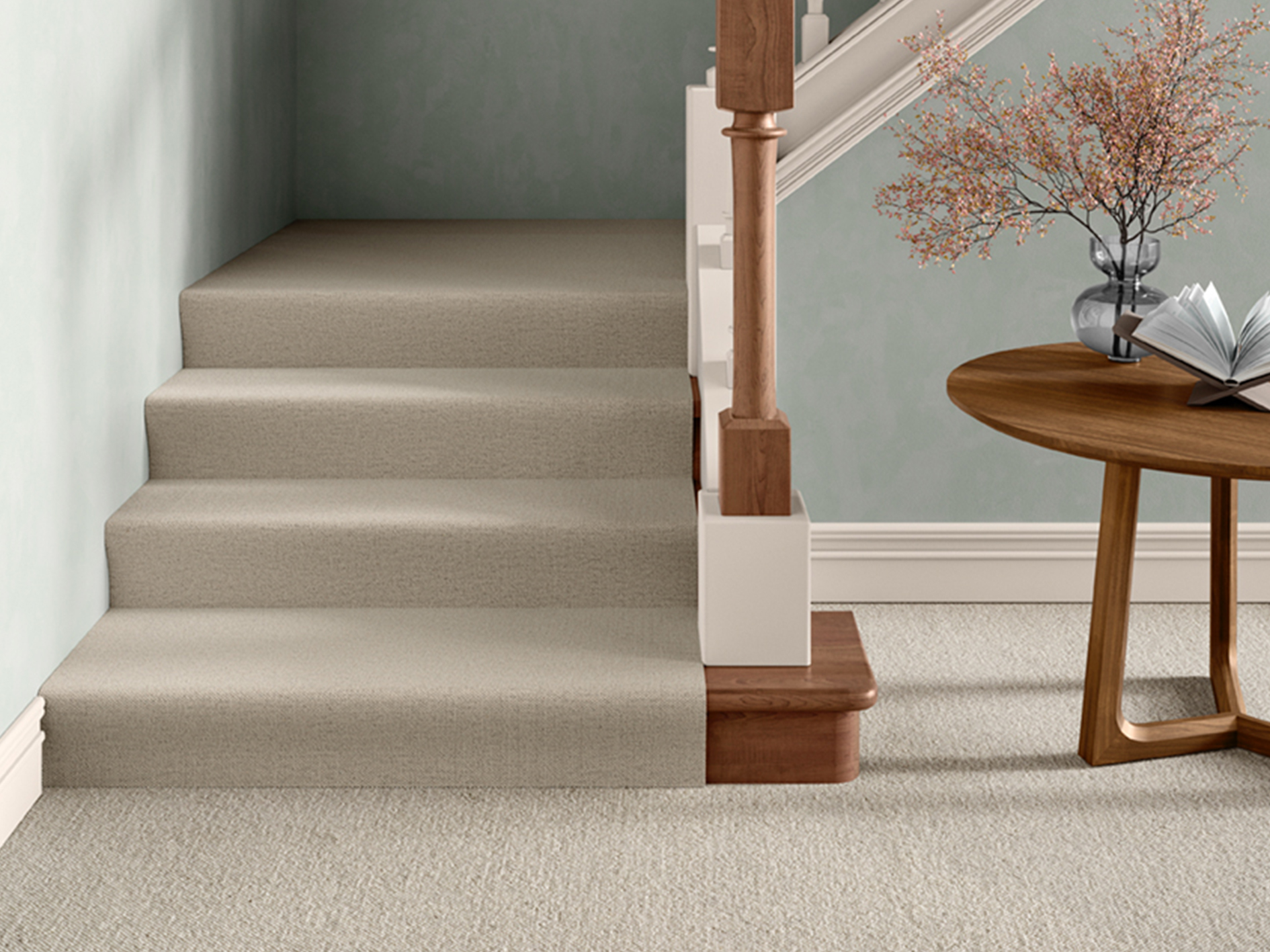 A modern hallway and staircase featuring a neutral beige carpet that continues seamlessly from the stairs onto the landing. The soft, textured pile complements the pale green walls and wooden accents, creating a calm and cohesive look, ideal for illustrating how to choose the right carpet for stairs and hallways.