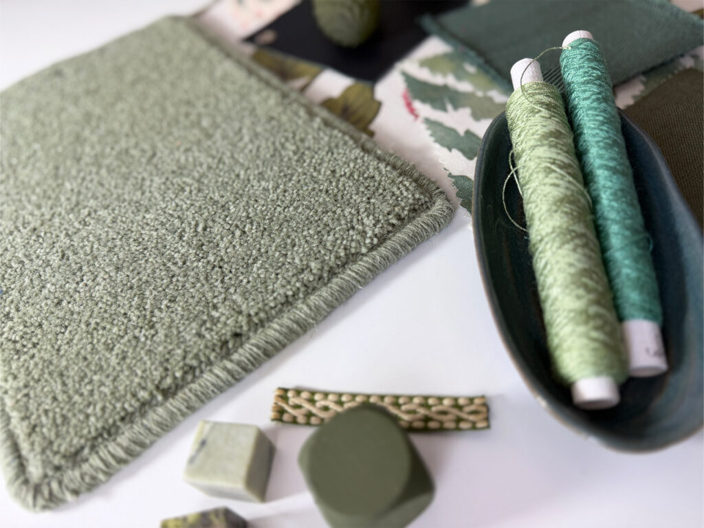 Close-up of Carpet Trends green carpet sample with coordinating threads, fabrics and accessories, showcasing texture and colour inspiration.