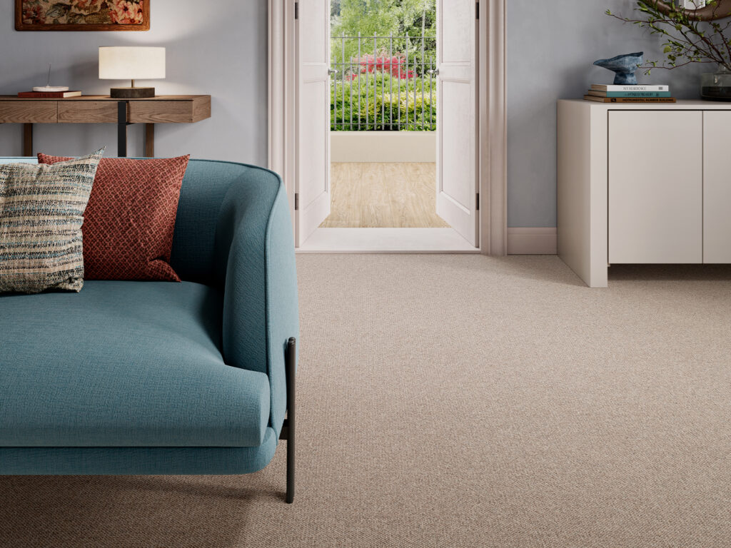 Stylish living room interior featuring Mayfair Weave, a soft beige woven carpet, teal sofa, patterned cushions, wooden console table and open doors to a balcony garden.