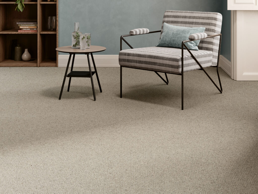 Light beige textured carpet in a modern living room with a striped lounge chair, round side table, wooden bookshelf, and teal accent wall.