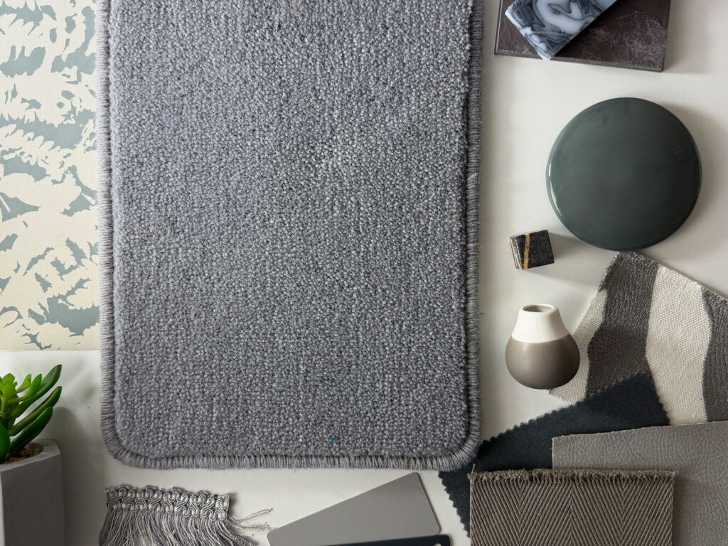 Luxury grey carpet sample with soft textured woven finish alongside contemporary interior design materials, showcasing premium bespoke carpeting for elegant homes, designer interiors and high-end residential flooring projects.
