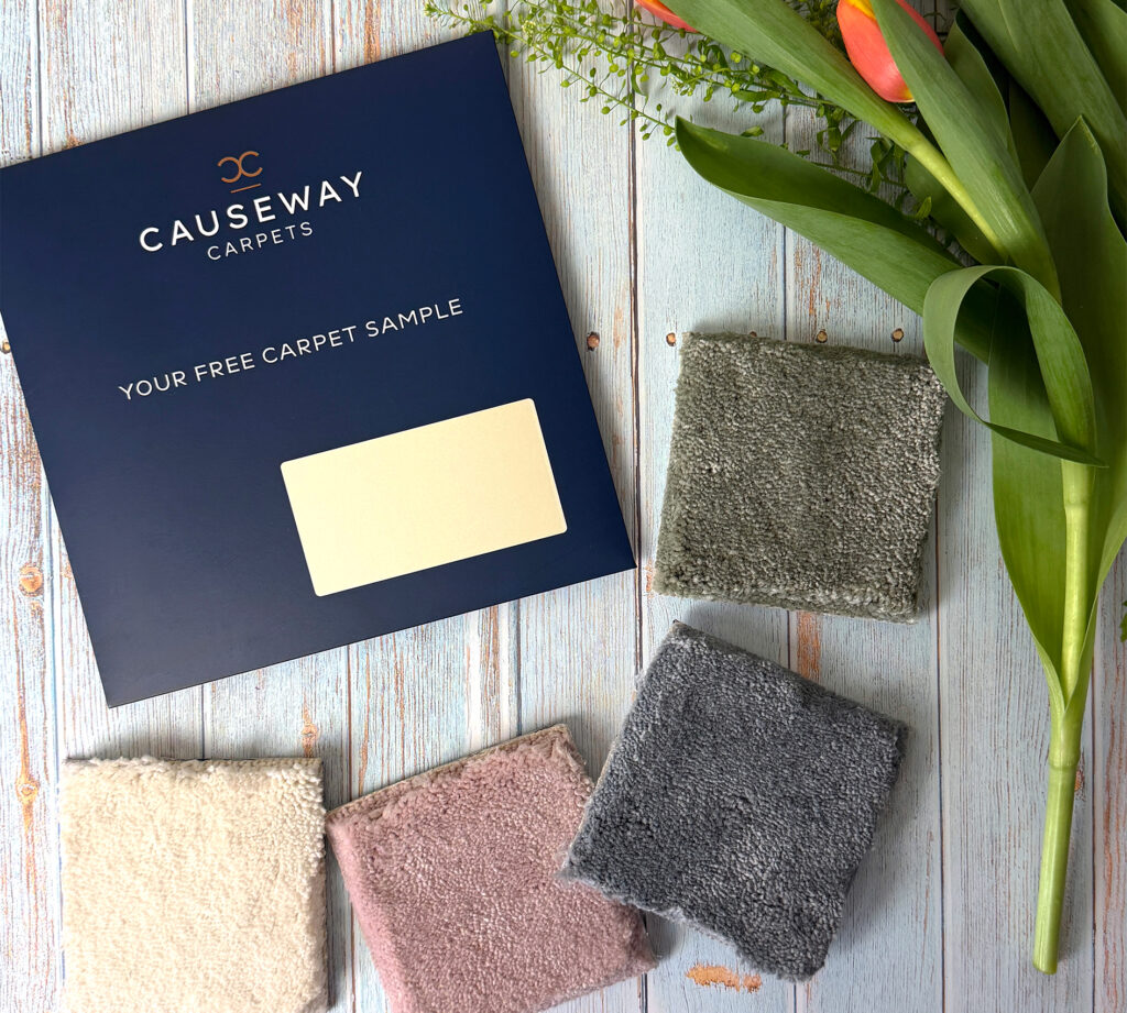 Luxury carpet sample pack with soft plush carpet swatches in cream, blush pink, grey and sage green tones beside fresh tulips, showcasing premium fitted carpets for elegant homes, modern interiors and high-end residential design.