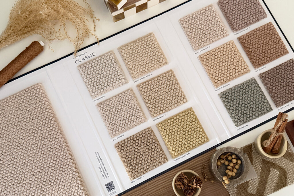 Camberley Classic carpet sample book displaying textured loop-pile carpet swatches in a palette of warm neutrals, earthy browns and muted green.