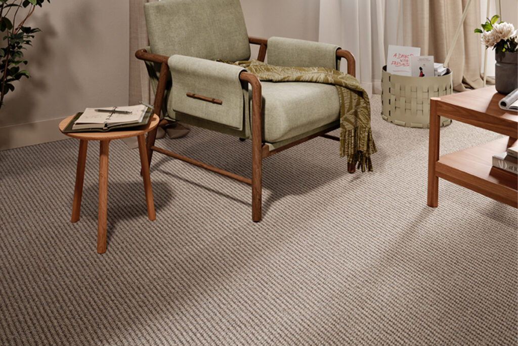 Textured neutral carpet in a contemporary living room with a pale green armchair, warm wooden furniture and floor-to-ceiling curtains.