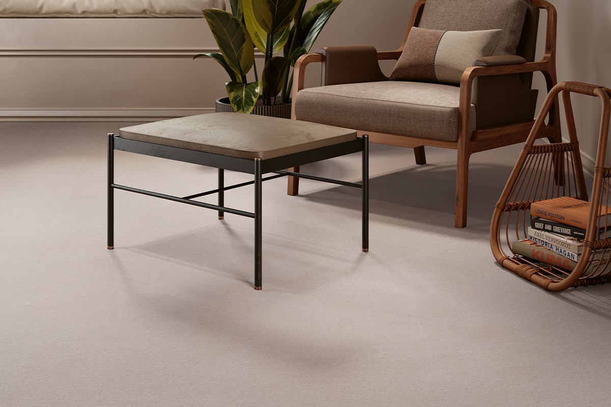 Neutral-toned living room featuring a soft cream carpet, wooden armchair, upholstered coffee table, houseplant and rattan magazine rack.